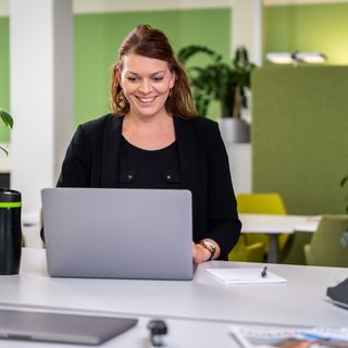 Mitarbeiterin der KOMSA steht am Arbeitsplatz und arbeitet am Laptop