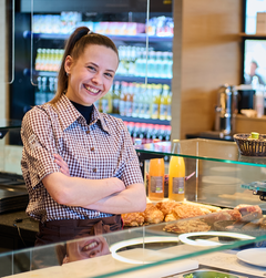 Auszubildende steht mit verschränkten Armen hinter der Snacktheke