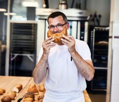 Mitarbeiter hält sich Croissant als Mund vors Gesicht