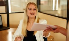 Mitarbeiterin sitzt am Schreibtisch und bekommt Unterlagen ausgehändigt