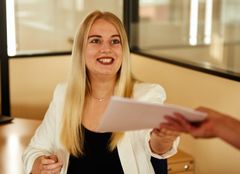 Mitarbeiterin sitzt am Schreibtisch und bekommt Unterlagen ausgehändigt