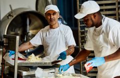 Mitarbeiter der Backstube belegen Kuchen an einer Anlage