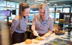 Ausbilderin erklärt Auszubildender das Brötchen belegen an der Snacktheke