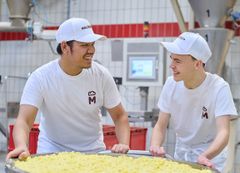 ein Praktikant und ein Azubi schieben einen Kessel in der Backstube mit Apfelstücken