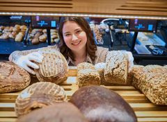 Praktikantin blickt freundlich durch das Brotregal