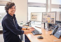 Auszubildender steht am Schreibtisch und schaut in die Kamera