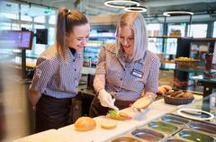 Ausbilderin zeigt einer Auszubildenden das perfekte Belegen von Brötchen