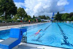 Schwimmbecken im Freibad mit einem Schwimmer, welcher krault. Im Hintergrund sieht man einen Sprungturm. 