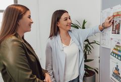 Zwei Mitarbeiterinnen vor einer Pinnwand