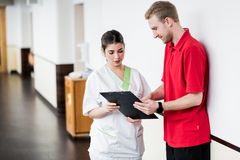 Eine Pflegerin und ein Therapeut sehen sich auf dem Gang gemeinsam eine Patientenakte an.