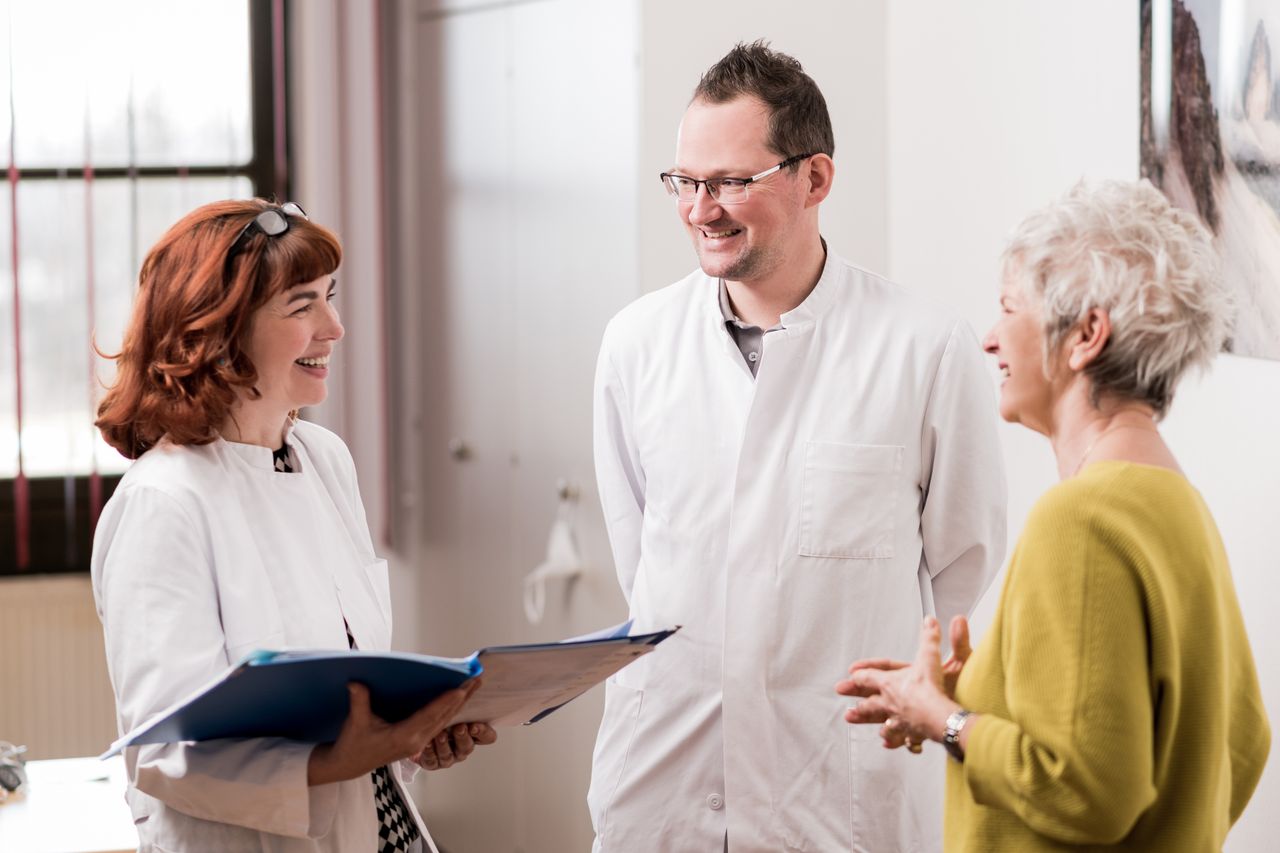 Zwei Ärzt:innen und eine Patientin stehen zusammen und lachen.