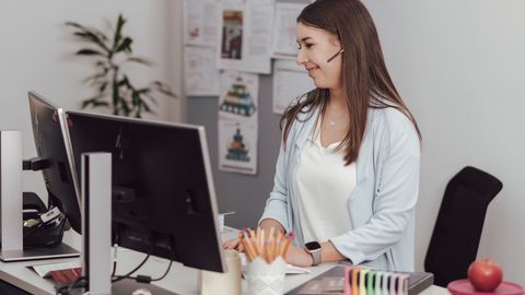 Eine Mitarbeiterin der Verwaltung sitzt am Schreibtisch, trägt ein Headset und arbeitet am Computer.