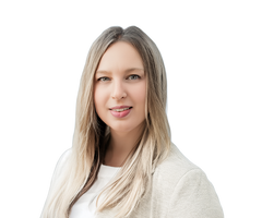 Eine Frau mit langen braunen Haaren lächelt in die Kamera. Sie trägt ein gemustertes Oberteil und eine braune Jacke.