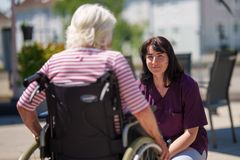 Pflegefachkraft auf Balkon einer Senioreneinrichtung lächelt Seniorin im Rollstuhl an – empathische Betreuung und soziale Teilhabe in der Altenpflege