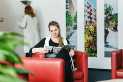 Eine Frau sitzt im im Wartebereich auf einem roten Sessel und ließt eine Zeitung