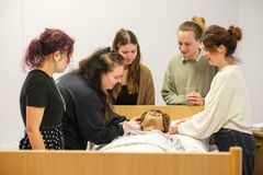 Eine Gruppe junger Menschen üben das Waschen von Patienten an einer Übungspuppe, die in einem Bett liegt.