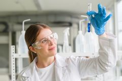 Pharmazeutisch-technische Assistentin im weißen Kittel hält Reagenzglas mit einer blauen Flüssigkeit hoch.