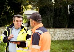 Zwei Monteure in Sicherheitswesten tauschen sich über Projekte und Fortgänge aus. 