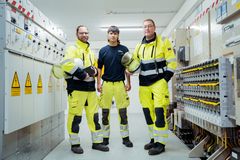 Drei Elektrofachkräfte in Uniform stehen vor einer großen Schaltanlage