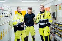 Drei Elektrofachkräfte in Sicherheitskleidung stehen vor Schaltanlagen 