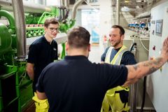 Drei Elektrofachkräfte stehen in Arbeitskleidung in Mitten einer großen BHKW-Anlage und diskutieren.