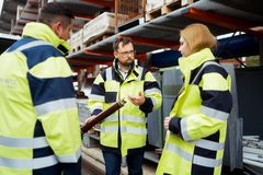 Zwei Eletroingenieure und eine junge rothaarige Elektroingenieurin in blau/gelben Sicherheitsjacken stehen vor dem Außenlager der REWAG. Der Eine hält eine große Sicherung in den Händen. Diese sieht aus wie eine Leuchtstoffröhre.