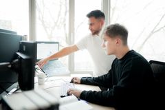 Ein junger Mitarbeiter erklärt einem Auszubildenden am Computer Arbeitsabläufe in der IT-Ausbildung.
