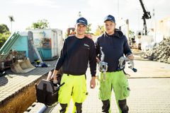 Zwei Auszubildende auf einer Baustelle tragen Werkzeugkoffer im Rahmen der Ausbildung zum Leitungsbauer für Infrastrukturtechnik.