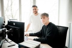 Ein junger Mitarbeiter erklärt einem Auszubildenden am Computer Arbeitsabläufe in der IT-Ausbildung.
