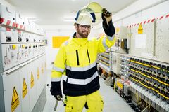 Elektrofachkraft steht mit Sicherheitsweste und Helm in einer Strom Schaltanlage.