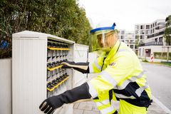 Eine Elektrofachkraft mit Sicherheitsanzug und Helm, arbeitet an einem Stromkasten in einem Wohngebiet.