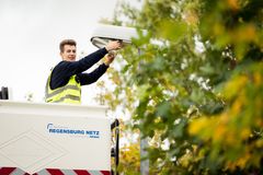 Ein junger Elektromonteur mit Sicherheitsweste, der in einem augefahrenen Korb eines Kranwagens der Regensburg Netz das Leuchtmittel einer Straßenlaterne wechselt.