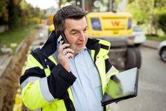 Ein Mitarbeiter der REWAG, mit Sicherheitsjacke bekleidet und einem Tablet in der Hand, telefoniert mit dem Handy vor Ort einer Baustelle. Der Austausch über Projekte und Fortgänge gehört zu den wesentlichen Tätigkeiten eines Baubeauftragten.