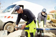 Zwei junge Männer in Arbeitskleidung, auf einer Baustelle, vor einem Einsatzfahrzeug der REWAG beim Verlegen eines Wasserleitungsrohres.