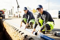 Zwei junge Männer in Arbeitskleidung der REWAG vor einem Graben, beim Verlegen einer Wasserleitung.