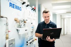 Das Bild zeigt einen Mann mit Rewag Uniform und Laptop in der Hand. Der Mann steht lächelnd vor einer Wand mit Zählanlagen, welche den Aufbau der Anlagen verdeutlichen soll