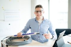 Das Bild zeigt einen Mann der in einem Büro steht und ein Kabel in der Hand hält während er lächelnd in die Kamera schaut
