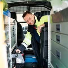 Dieses Bild zeigt einen lächelnden Mann mit Sicherheitsweste, der aus dem Auto schaut, welches er im Dienst fährt.