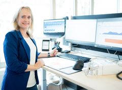 Dieses Bild zeigt eine Frau am Schreibtisch, vor mehreren Monitoren bei ihrer Arbeit