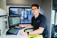 Dieses Bild zeigt einen Mann in Rewag Uniform, wie er am Schreibtisch vor einen Bildschirm sitzt und in die Kamera lächelt. Das Bild soll die Arbeit bei der REWAG verdeutlichen