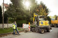 Baustelle mit zwei Baggern bei der Stromleitungen in der Erde verbaut werden. Ein Bauleiter in gelber Sicherheitsjacke der REWAG telefoniert gerade mit dem Handy.