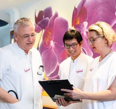 Zwei Ärzte schauen sich mit einer Pflegefachkraft eine Patientenakte an