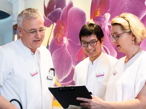 Zwei Ärzte schauen sich mit einer Pflegefachkraft eine Patientenakte an