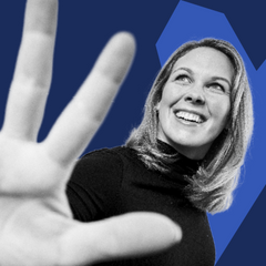 Eine lächelnde Frau blickt nach oben, während sie eine Hand in den Vordergrund ausstreckt; das Bild ist in Schwarz-Weiß gehalten mit blauem grafischen Hintergrund.