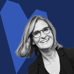 Eine lächelnde Frau mit Brille blickt in die Kamera; das Bild ist in Schwarz-Weiß gehalten mit blauem grafischen Hintergrund.