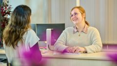 Zwei Frauen stehen sich an einem Tisch im Büro gegenüber, unterhalten sich lächelnd und besprechen ein Dokument.
