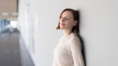 Frau lehnt gegen eine Wand und atmet mit geschlossenen Augen ein