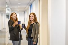 Büro Szene: Zwei Frauen stehen auf dem Flur in einem Büro mit Kaffeetassen in der Hand