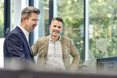 Zwei Männer in Anzügen unterhalten sich stehend in einem Büro