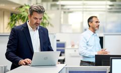 Büro Szene mit zwei Männern, einer arbeitet im Vordergrund am Laptop